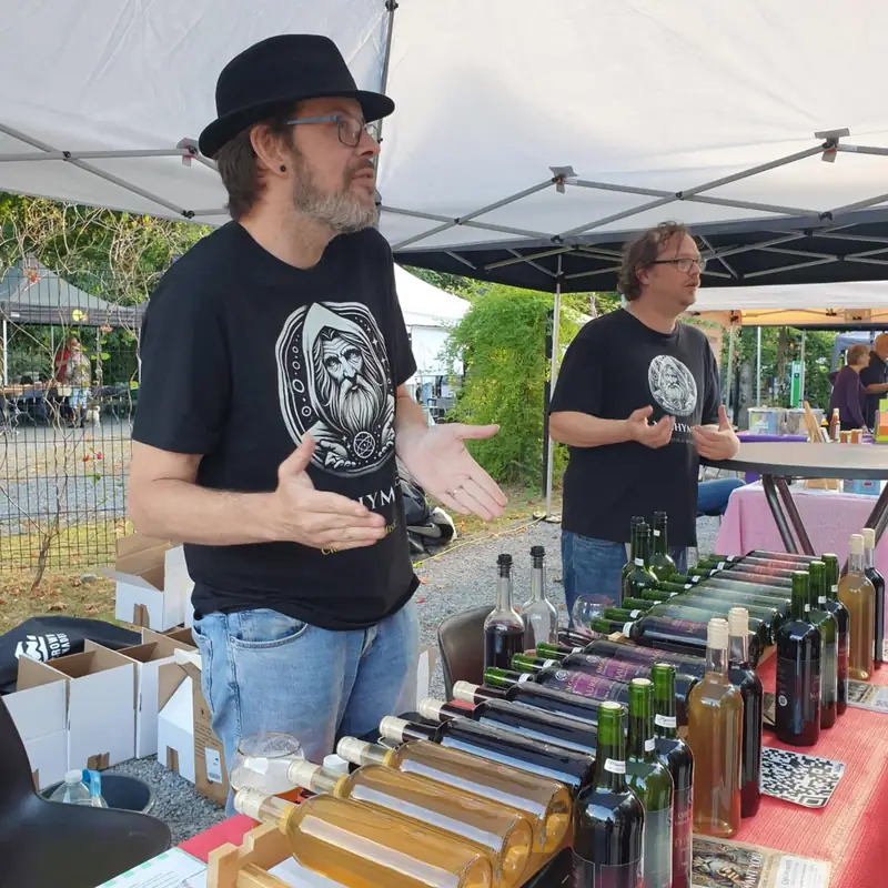 L'équipe de L'Alchymiste derrière son stand, bouteilles alignées sur la table